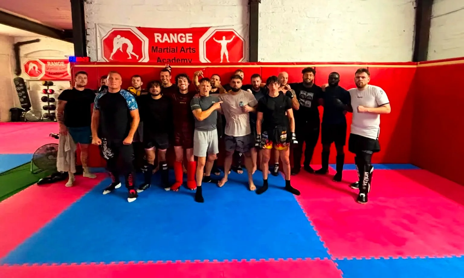 A full class of adults standing together on the mats at Range Martial Arts Academy, under the academy banner