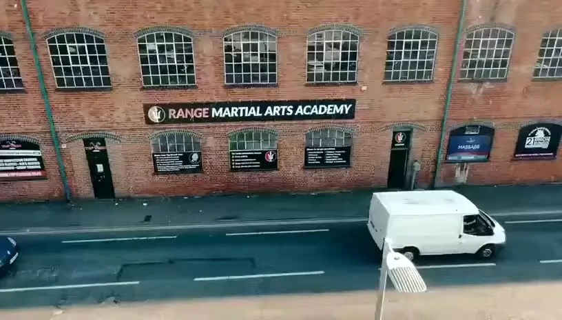 Two members drilling a takedown on the mats at Range Martial Arts Academy, with a coach watching