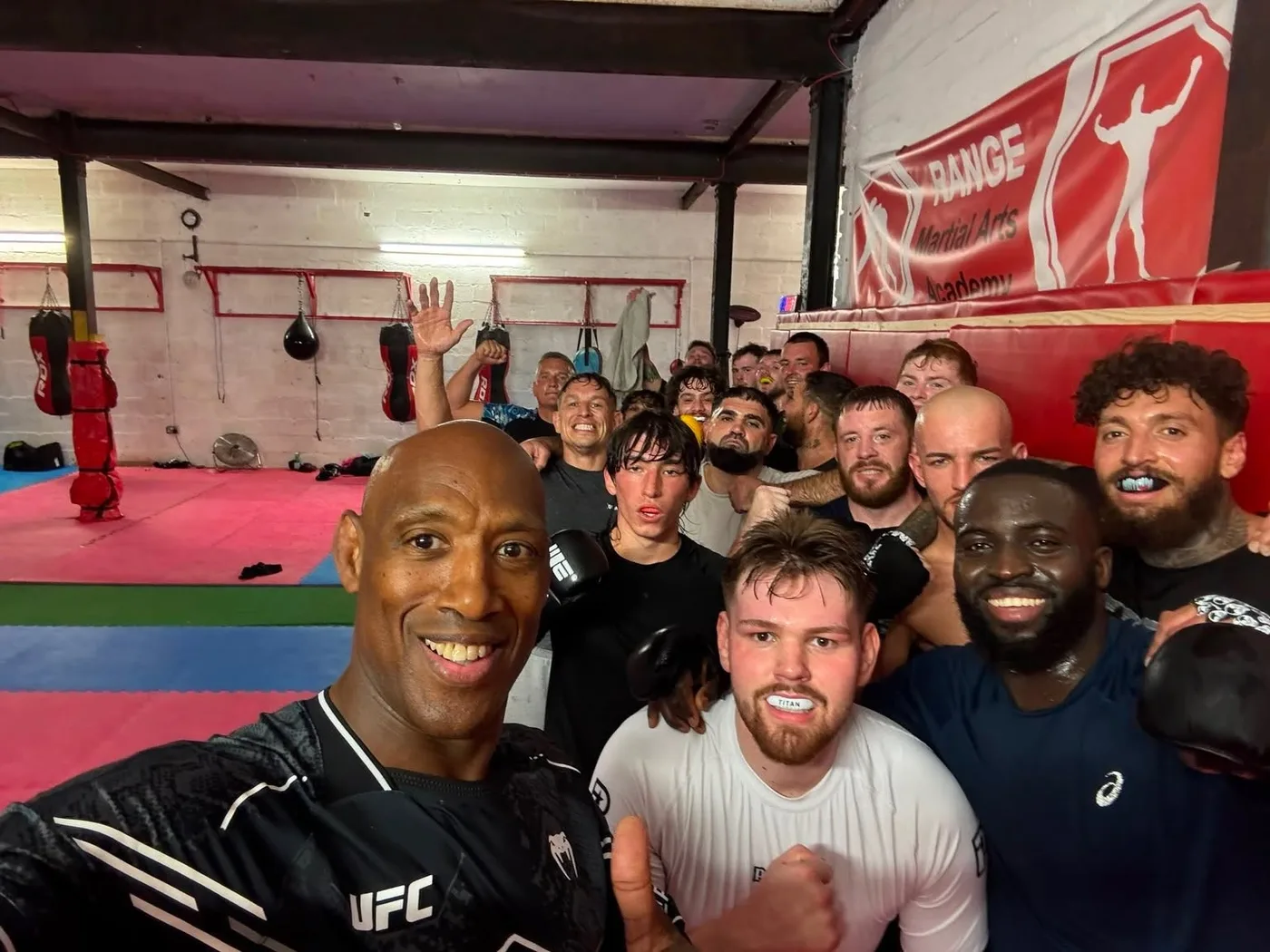 Mark Weir and the class crowded together for a photo after a session, gloves on and punch bags behind them
